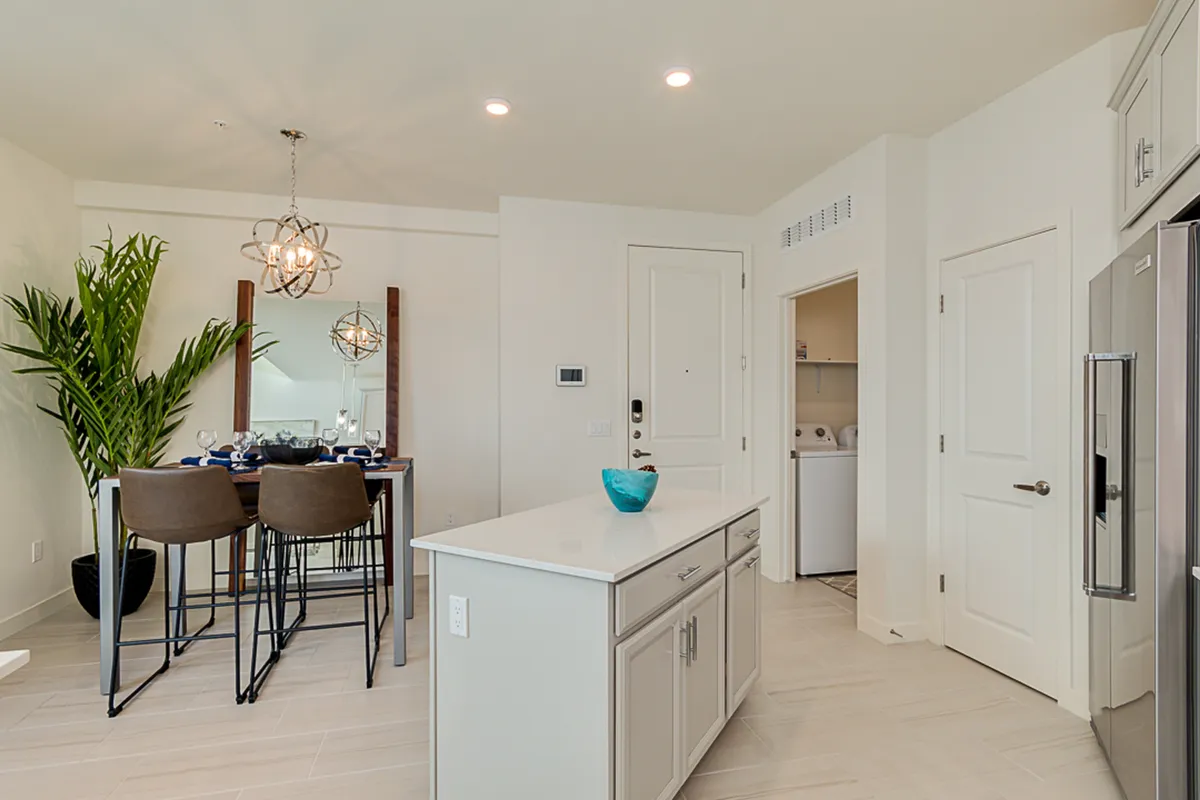 The dining area and kitchen island are bathed in warm, natural light, with a decorative plant and elegant lighting fixtures creating a welcoming mood. The image focuses on areas perfect for casual dining, cooking, or hosting special occasions.