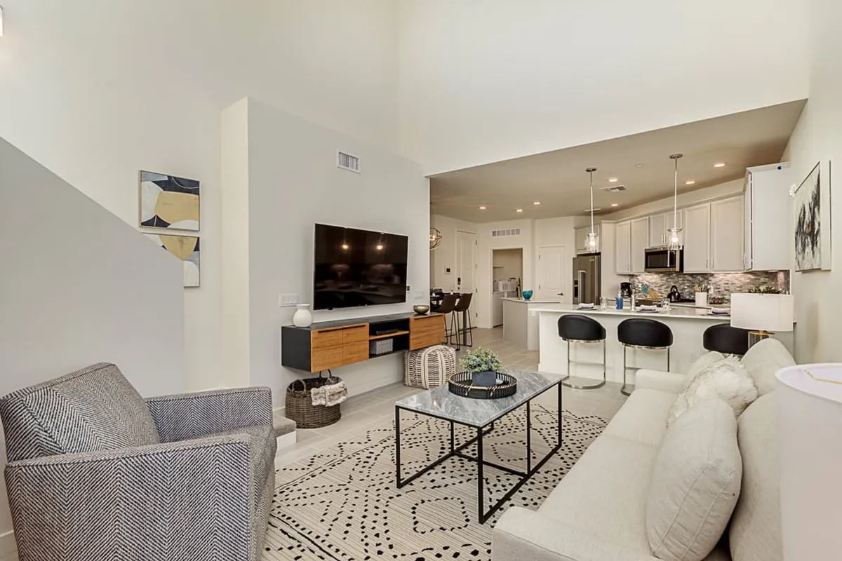 A stylish open-concept living area featuring a plush sofa, coffee table, television, and a kitchen area in the background. The space is inviting for both relaxation after work and entertaining guests or colleagues, with ample room for unwinding or networking.
