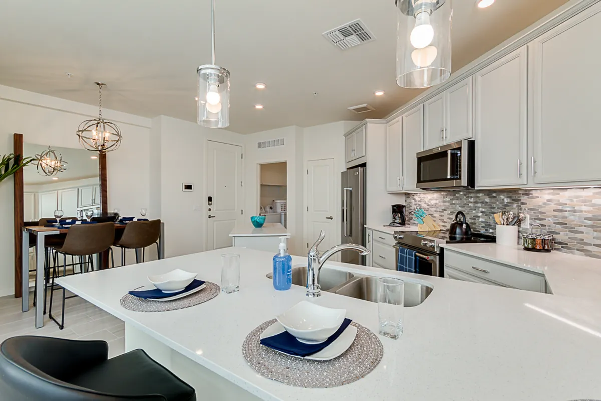 A stylish kitchen with a central island leading directly to the dining area. Decorative light fixtures hang overhead, and modern appliances complete the space, providing both form and function.
