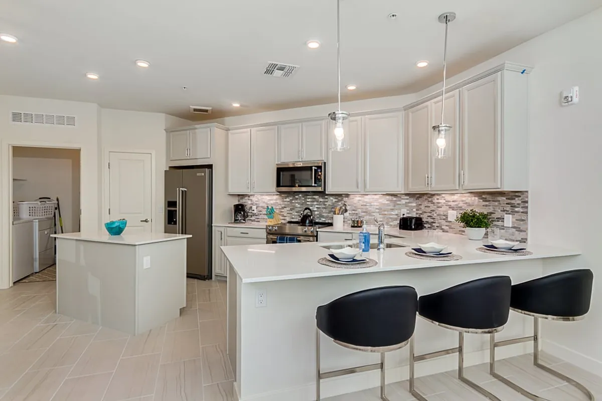 A contemporary kitchen featuring a spacious island with bar stools, gleaming stainless steel appliances, a stylish backsplash, and abundant natural light streaming through windows. The layout is open, seamlessly connecting to adjacent living and dining spaces.