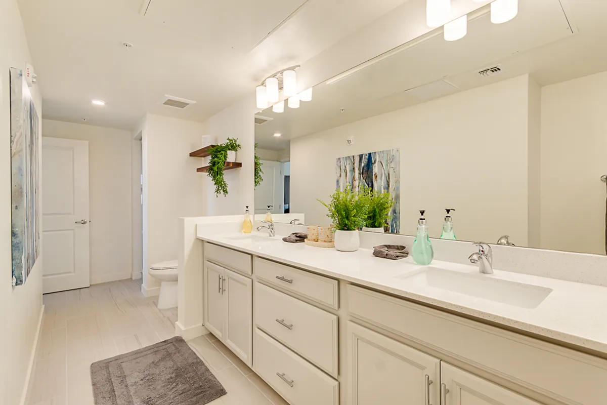A modern bathroom with a double sink vanity, decorative wall art, green plants, and contemporary lighting fixtures. The design is both luxurious and tranquil, ideal for pampering sessions and peaceful routines.