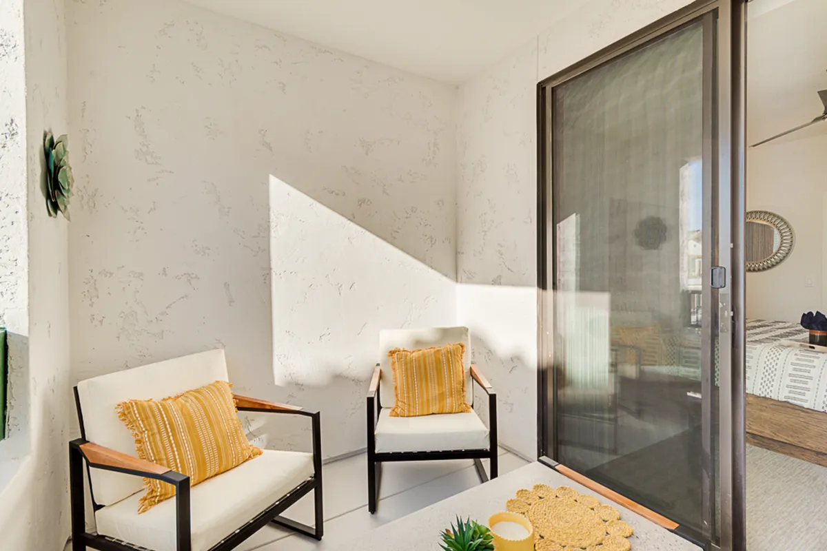 A calm and welcoming interior featuring two armchairs with decorative pillows, set against a textured wall and woven rug. The space suggests casual conversations, relaxed coffee breaks, and a warm ambiance, enhanced by natural light.